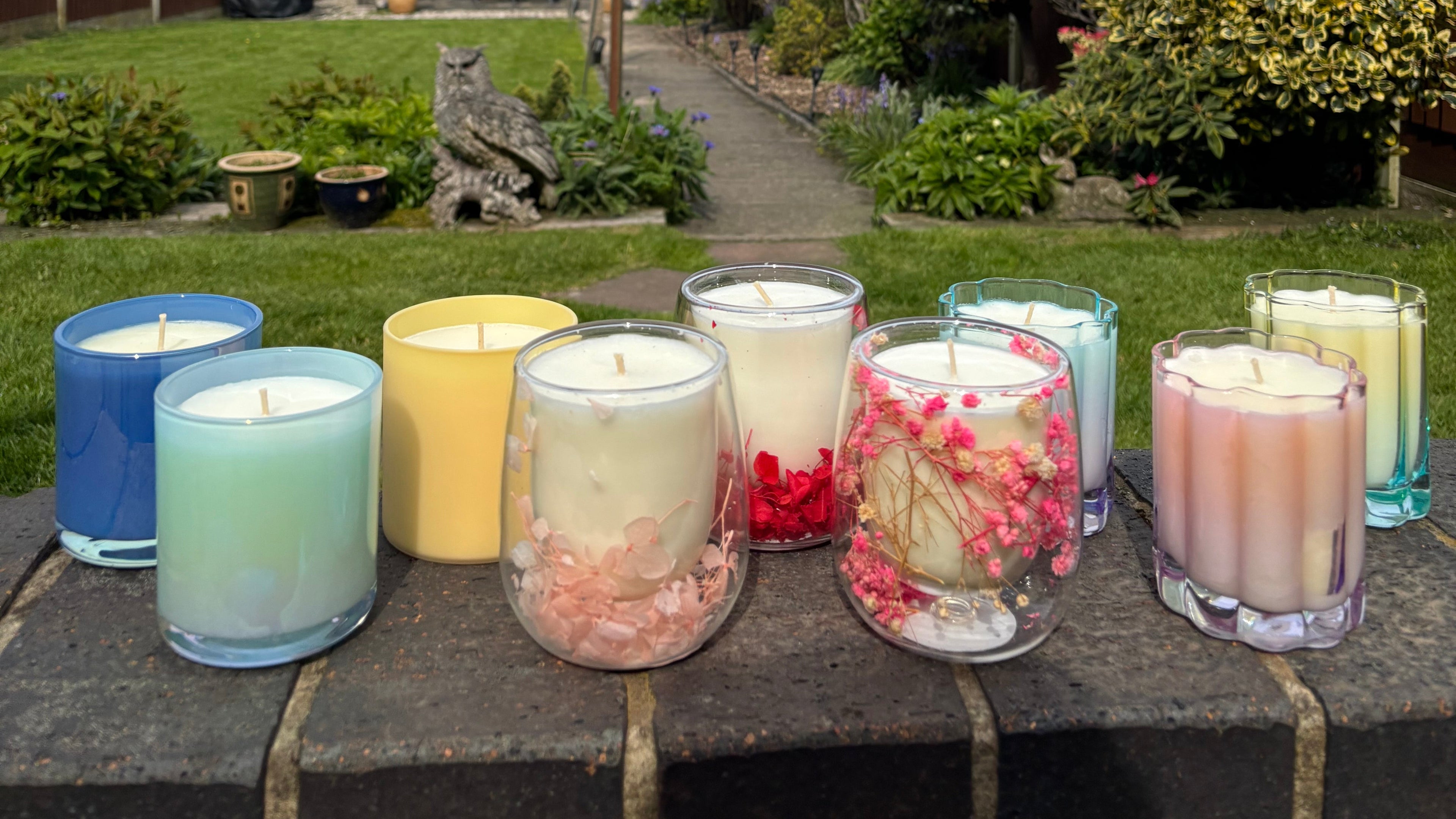 Colorful candles in glass holders on a stone surface with a garden background